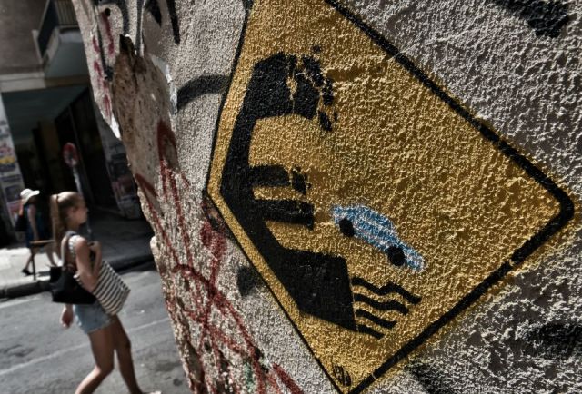 A woman walks past a wall bearing graffitti concerning Greece's possible exit from the Euro in Athens on June 28, 2015.  The European Central Bank was set to hold emergency talks on June 28, 2015 on whether to keep or cut its financial lifeline to Athens, as France warned of a "real risk" Greece will leave the euro. After talks in Brussels broke down in acrimony Saturday between Athens' left-wing leaders and the rest of the eurozone, Greece hurtled toward default with its EU-IMF creditors, left solely reliant on emergency cash from the ECB.  AFP PHOTO / ARIS MESSINIS